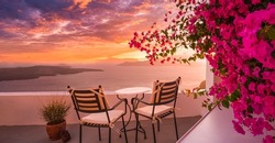 Summer sunset vacation scenic of luxury famous Europe destination. White architecture in Santorini, Greece. Stunning travel scenery with pink flowers chairs, terrace sunny blue sky. Romantic street