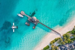 Beautiful aerial view of Maldives shore, jetty villa seaplane top view, wooden boat Dhoni and tropical beach. Palm trees white sand, sea. Luxury travel and vacation concept. Amazing aerial landscape