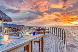 Amazing romantic dinner tables in outdoors beach restaurant. Wooden deck with candles under sunset sky. Vacation, honeymoon romance love, luxury destination dinning, exotic table setup with sea view