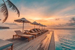 Tropical sunset over outdoor infinity pool in summer seaside resort, beach landscape. Luxury tranquil beach holiday, poolside reflection, relaxing chaise lounge romantic colorful sky, chairs umbrella
