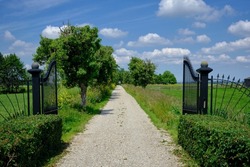A gravel driveway of a country property. Viewed through black wrought-iron gates.