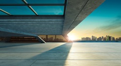 Perspective view of empty concrete floor and modern rooftop building with sunset cityscape scene. Mixed media