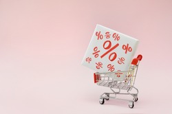 Image of empty shopping trolley or cart with box of discount percent sale black Friday products on pink background. Concept of sell or buy with place for your text