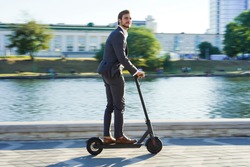 Young business man in a suit riding an electric scooter on a business meeting. Ecological transportation concept