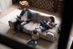 Gadgets addiction. Young family of three holding and using different electronic devices while sitting on sofa in the living room. Father and their daughters with modern gadgets