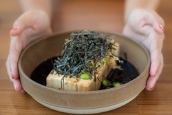 Close-up a cold Tofu with dashi soy sauce, Topping seaweed and edamame in a Japanese style earthenware bowl with a woman's hand holding a bowl.