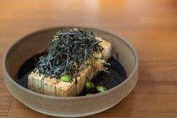 Close up cold Tofu with dashi soy sauce, Topping seaweed and edamame in a Japanese style earthenware bowl.