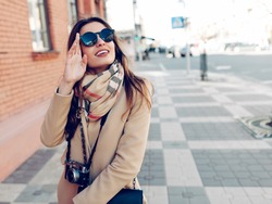Beautiful and young girl in a coat and scarf and sunglasses walking around the city in the summer.