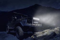 Night photo of the Off-road SUV with headlights high in the mountains