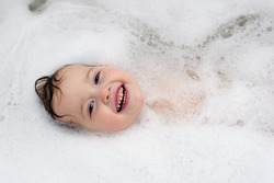 Smiling happy baby is swimming in foam in bath