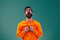 desperate man screaming out loud putting his fist hands to his chest - caucasian person with orange sweater on green background