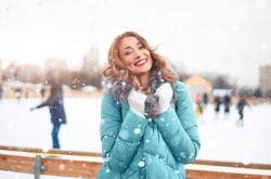 Beautiful lovely middle-aged girl curly hair warm winter jackets white glove stands ice rink background Town Square. Christmas mood lifestyle Happy holiday woman walk snowy day Winter leisure 