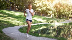 Woman running road summer park near lake Active sporty caucasian female morning workout Healthy lifestyle concept. Athletic person sportswear exercises Dressed white t-shirt full length
