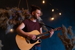 Male musician playing acoustic guitar. Guitarist plays classical guitar on stage in concert Handsome young hipster male guitar player perform private party Stylish long hair Medium shoot