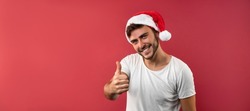 Young handsome guy in a white t-shirt and Santa hats stands on red background 