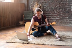 Man acoustic guitar sitting floor with laptop and headphones online music lessons. Caucasian young guitar player practicing musical instrument 