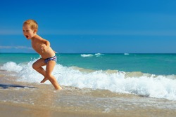cute child running from sea  waves on beach