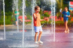 excited boy having fun between water jets, in fountain. Summer in the city