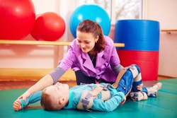 cute kid with disability has musculoskeletal therapy by doing exercises in body fixing belts