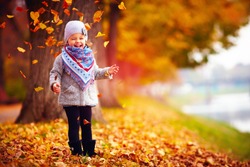 beautiful happy baby girl having fun in autumn park, among fallen leaves