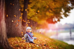 adorable happy baby girl throwing the fallen leaves up, playing in the autumn park