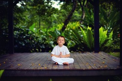 cute little baby boy, kid meditating in rainy forest park, sitting on wooden decks