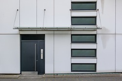 Front view on sidewalk of typical facade with swing door, canopy and windows at the entrance of residential building in Europe.
