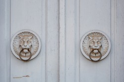 Detail of two white antique tiger or lion bas relief sculptures and metal door knocker's rings on wooden white door.