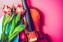 Close-up of wooden handmade musical instrument with fresh bouquet of flowers on pink background. Joy of art and nature. Romance, music and artistry concept, copy space