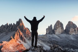 Man conquering the hill and show hands while standing on the stone in the front of Paternkofel and Tre Chime mountains