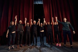 People bowing to audience. Group of actors in dark colored clothes on rehearsal in the theater.