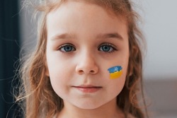 Close up view. Portrait of little girl with Ukrainian flag make up on the face.