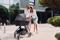 Talking and having fun. Two female friends having a walk with baby carriage outdoors.