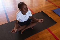 High angle view of black schoolboy doing yoga and meditating on a yoga mat in school