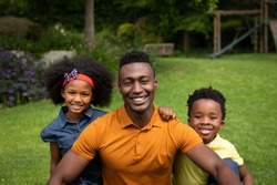 Portrait of a smiling African American man in the garden with his daughter and son looking to camera.. Social distancing and self isolation in quarantine lockdown for Coronavirus Covid19
