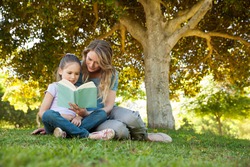 Full length of a mother and daughter reading a book at the park