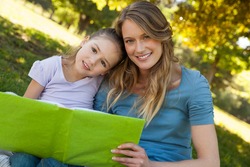 Portrait of a happy mother and daughter reading a book at the park