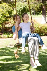 Full length of a happy mother and daughter sitting on swing at the park