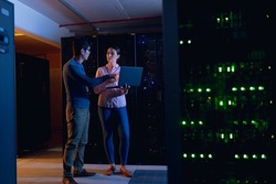 Diverse male and female engineers using laptop in computer server room. database server management and maintenance concept
