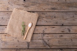 Directly above shot of rock salt in wooden spoon and rosemary on jute fabric at table. unaltered, copy space, ingredient, food, herb, rock salt and seasoning.