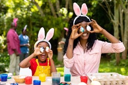 Happy african american girl and mother playing with easter eggs while family in background. unaltered, lifestyle, easter day, art, celebration, family, cultures and holiday concept.