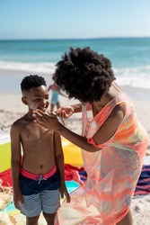 African american mother applying suntan lotion on son's cheek while enjoying summer holiday at beach. unaltered, family, lifestyle, togetherness, enjoyment and holiday concept.