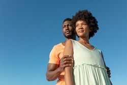 Low angle view of african american couple standing against clear blue sky with copy space. unaltered, lifestyle, love, togetherness and holiday concept.