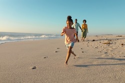 Happy african american girl running on sand against parents walking at beach. unaltered, family, lifestyle, togetherness, enjoyment and holiday concept.