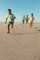 Happy african american siblings running against parents walking at beach on sunny day. unaltered, family, lifestyle, togetherness, enjoyment and holiday concept.