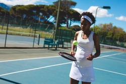 African american young female athlete playing with ball and racket at tennis court on sunny day. unaltered, sport, competition and tennis game concept.