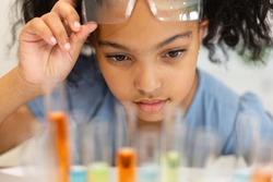 Close-up of biracial elementary schoolgirl looking at chemicals in test tubes during chemistry class. unaltered, education, learning, scientific experiment, stem, protection and school concept.