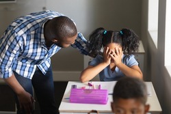 African american young male teacher consoling sad biracial elementary schoolgirl sitting at desk. unaltered, education, communication, childhood, sadness, depression, failure and school concept.