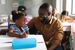 Smiling african american young male teacher looking at african american elementary schoolgirl. unaltered, education, childhood, disability, learning, physical disability and school concept.