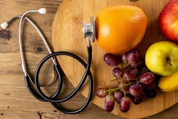 Directly above shot of apples with orange and grapes on wooden tray by stethoscope on table. unaltered, healthy food, fresh, diet, medical, heart, disease and healthcare concept.
